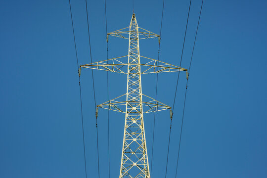 Single high voltage electricity pylon or transmission tower and power lines low angle view against clear blue sky as energy topic.