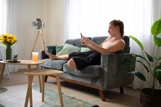A white woman sits on a sofa using her smartphone