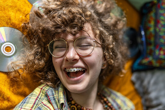 A teenage girl with curly hair laughs indoors while enjoying music