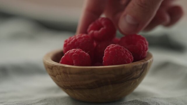 Slow motion man hand put fresh ripe raspberries in a small wooden bowl