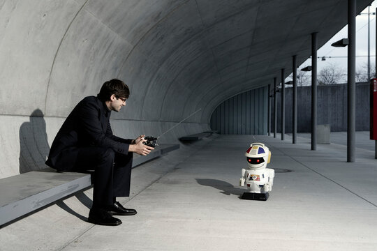 Businessman sitting outdoors playing with a toy robot