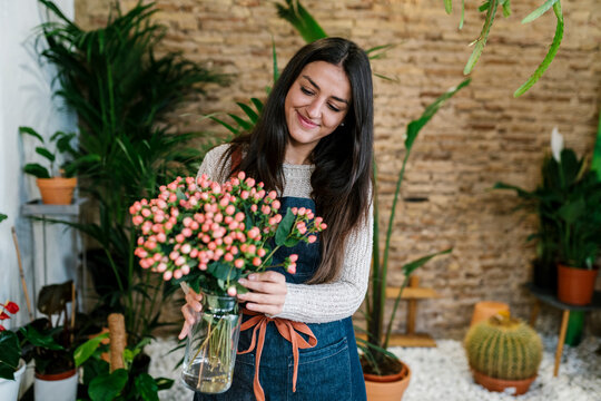 Smiling young female florist holding Hypericum flower vase at shop