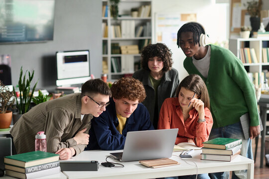 A diverse student group looks at a laptop screen in the library