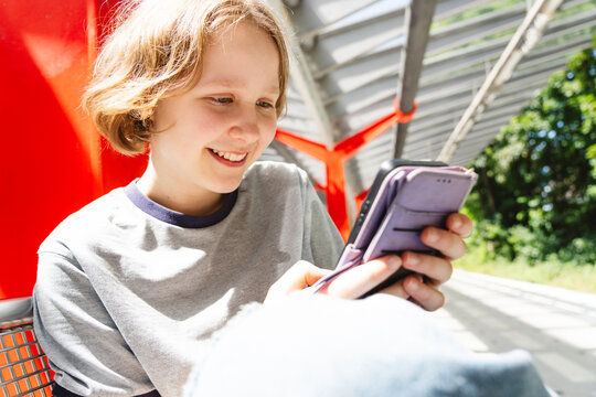 A smiling girl uses her smartphone at a public transport stop