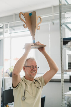 Smiling doctor holds a cardboard cup indoors to celebrate success