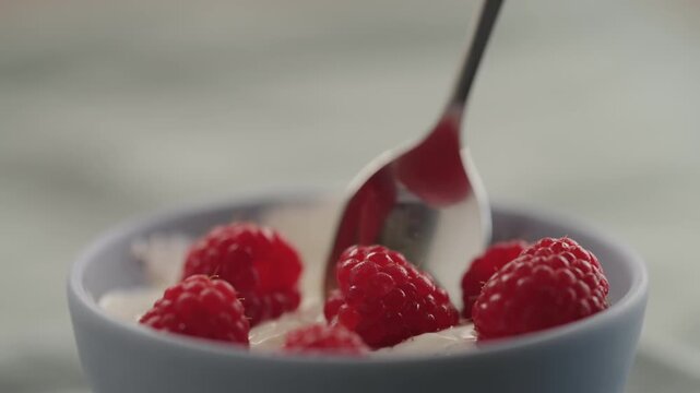 Slow motion taking a spoon of raspberries with yogurt from a bowl