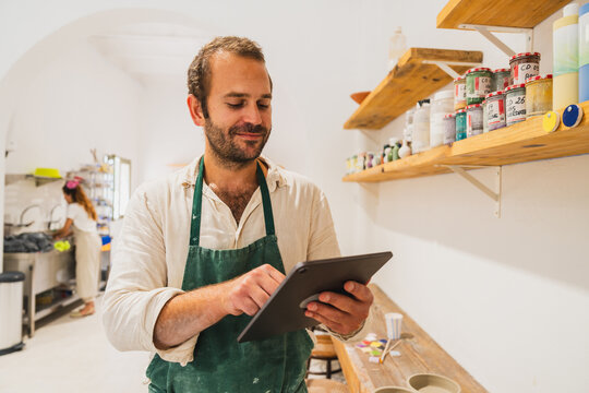 Male artisan uses a tablet for inventory in a pottery studio