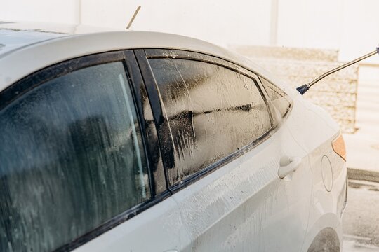 A pressure washer sprays water onto a white car outdoors