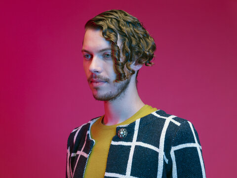 Portrait of fashionable dressed young man with curly hair in front of red background