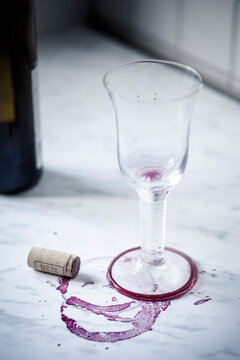 Empty red wine glass, bottle, stains and wine cork on white marble