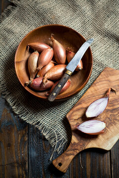 Shallots, Allium ascalonicum, in wooden bowl with knife, studio
