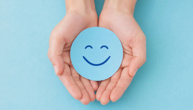 Hands holding a blue paper circle with a smiling face during a bright studio lighting for mental health concept