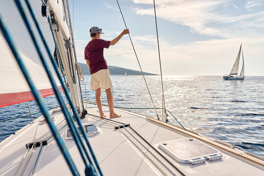 A young boy stands on a sailboat deck looking at the ocean