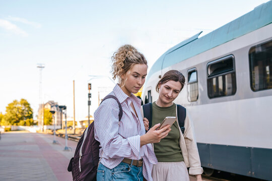 Female friends look at a smartphone at the train station