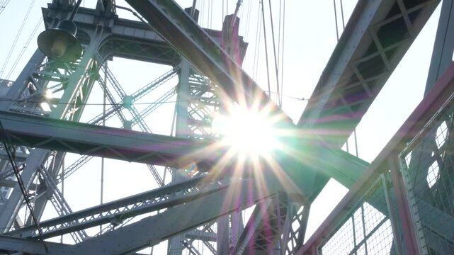 Williamsburg Bridge from Manhattan to Brooklyn, New York City, USA. Architecture of United States, tourist landmark. Metallic cable-stayed bridge. Sun rays and sky from pedestrian path. Low angle.