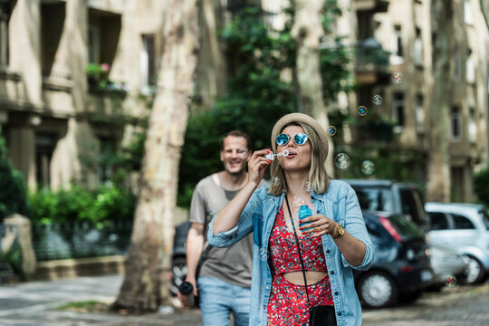A woman blows a soap bubble while walking with a man in the city