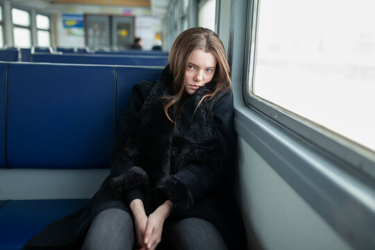 Young woman in a fur coat sitting on a commuter train during winter