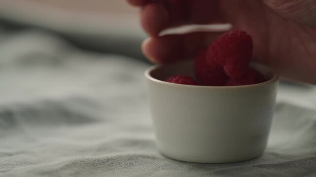 Slow motion man hand put fresh ripe raspberries in a white small bowl