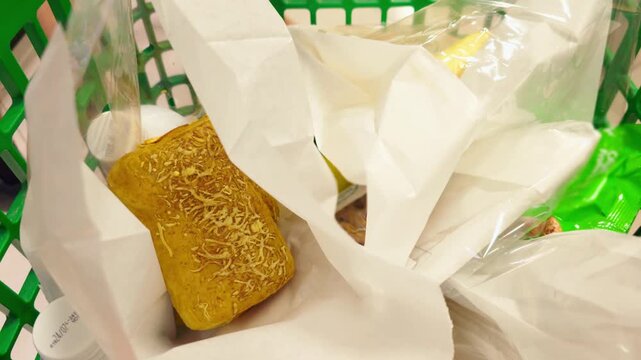 Supermarket shopping cart moving through grocery store with fresh bread and packaged food. Green basket with groceries during retail shopping trip. Everyday food shopping and consumer lifestyle