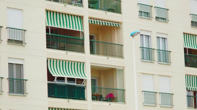 Spanish apartment building with security bars and roller shutters. Residential balconies with striped awnings on urban facade. Anti squatter home protection and property security in Spain