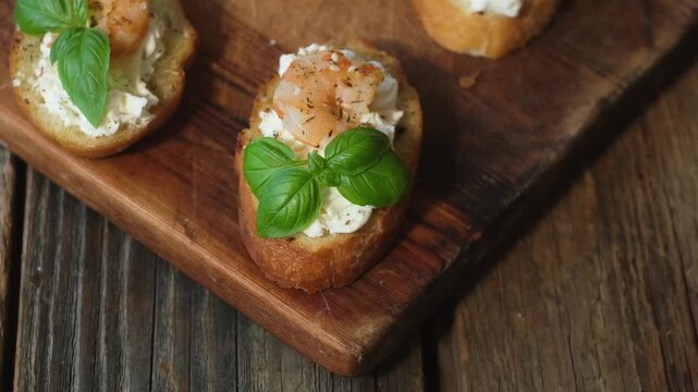 Bruschetta or crostini with cream cheese, shrimp and fresh basil on wooden board. Tasty snacks.
