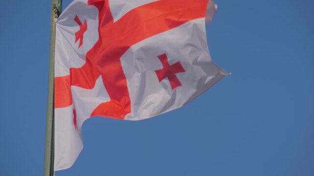 Colorful Georgian flag is fluttering in the wind against clear blue sky in Georgia. Concept of diplomacy, international affairs, politics, freedom, and patriotism