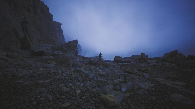 Distant stone sentinel on scree slope, small stacked rocks framed by wide moody sky, gritty texture and low light convey resilience and isolated landmark