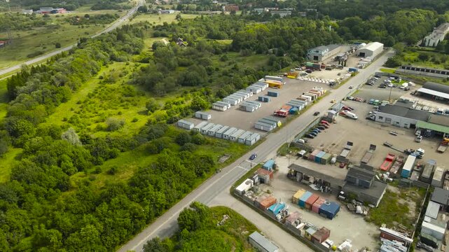 Industrial warehouse and logistics park next to a lush green forest, showing a stark contrast between nature and industry with cars driving on a road separating the two distinct zones