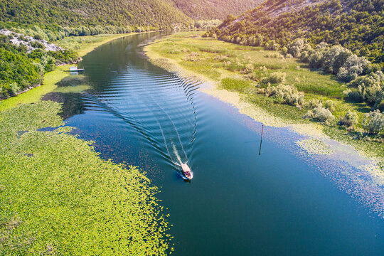 Small boat leaving ripples while navigating the winding Rijeka Crnojevica river, surrounded by lush green mountains and water lilies