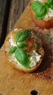 Vertical video. Bruschetta or crostini. Toasted baguette slices with feta cream cheese, shrimp and fresh basil on wooden board. 