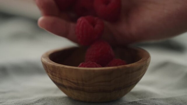 Slow motion man hand put fresh ripe raspberries in a small wooden bowl