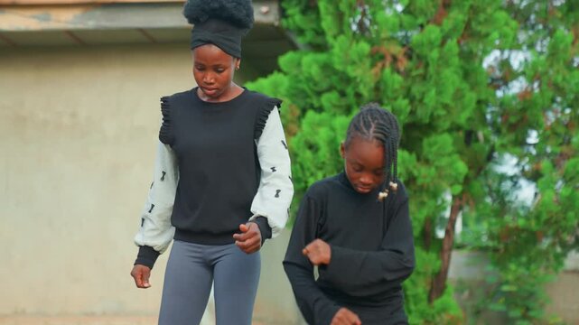 Black mother and child practicing together in yard, patient coaching and gesture exchange, step guidance and mimicry, suburban fence and tree backdrop, supportive family interaction