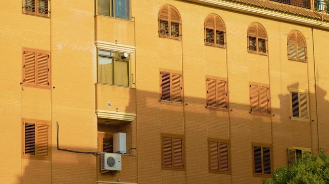 Protective window shutters and wooden security screens across Spanish brick building. Residential architecture with restricted exterior access. Anti squatting measures and property protection