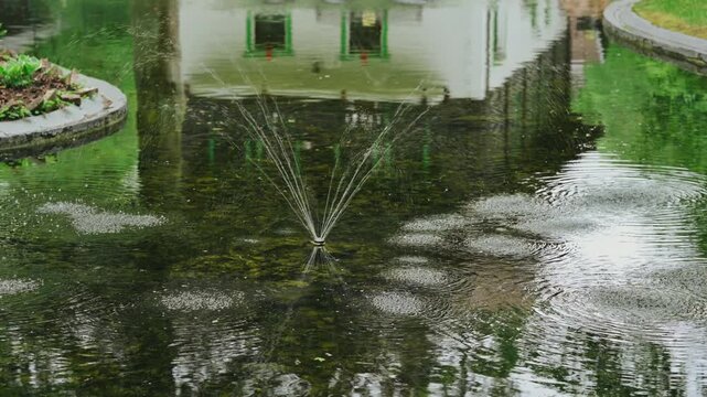 water fountain spraying water, in garden or park setting with greenery and a, with green, white accents.