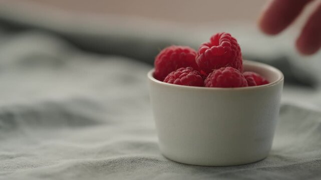 Slow motion man hand put fresh ripe raspberries in a white small bowl