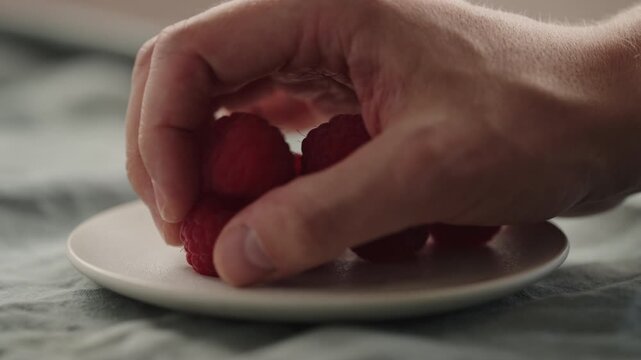 Slow motion man hand put fresh ripe raspberries on a white saucer