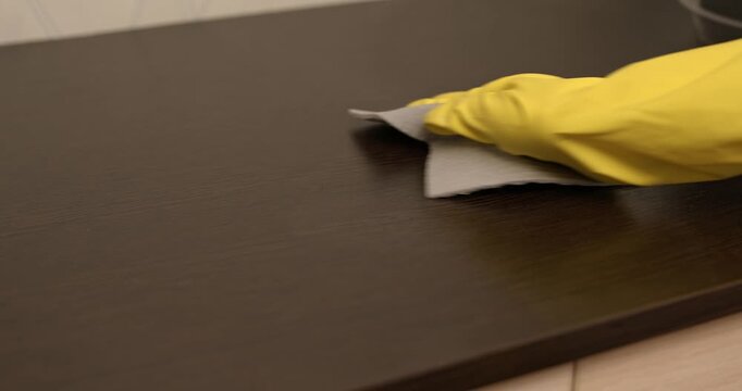 Home cleaning process, dust wiped off the cabinet, hand in yellow gloves cleaning the cabinet with a cloth.