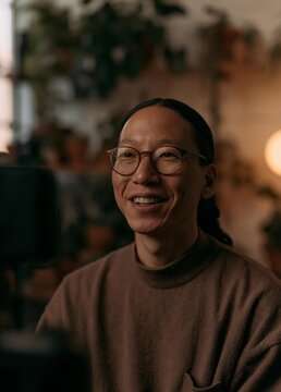 Portrait of a middle-aged asian woman with a big smile on her face. she is wearing glasses and a brown sweater.