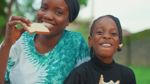 Joyful family moment. Playful backyard scene with smiling family. Happy mother and child bonding over bread outdoors. Candid image of mother and child giggling while sharing bread in yard