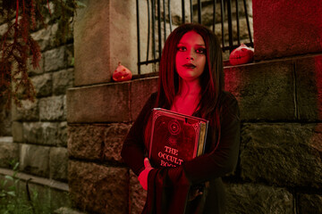 Obraz premium Portrait of Caucasian teenager girl wearing witch costume holding occult book during Halloween celebration outdoors. Image suitable for seasonal marketing campaigns and event promotions