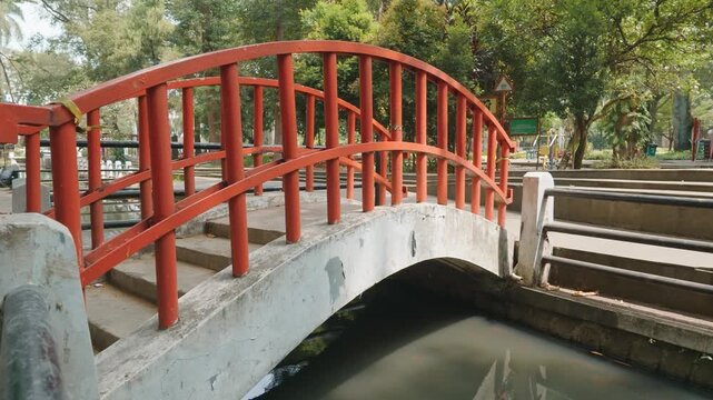 Charming red arched footbridge over a small canal in a public park.