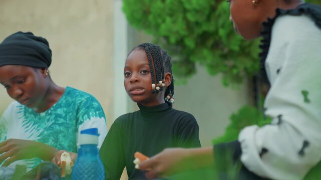 Waiting and sharing african mother child with sibling nearby, trio on courtyard bench exchanging food and glances, subtle expressions of hope and patience, hands passing bread, everyday family routine