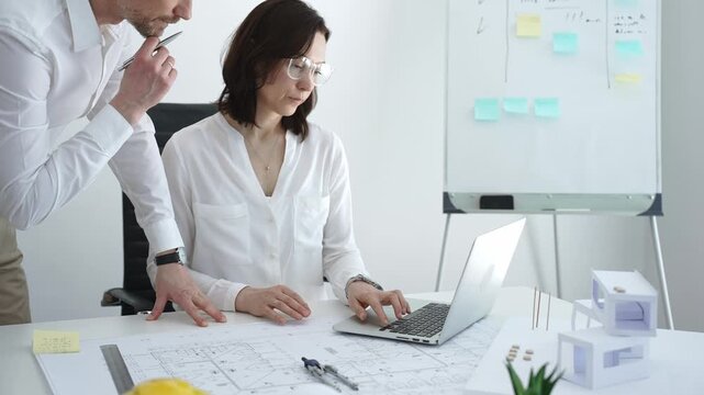 Architects collaborating on building design, reviewing blueprint plans and architectural models, creating detailed floor layout sketches in a professional office environment