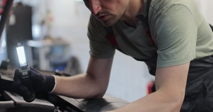 Close up mechanic man with lamp working at workshop. concept car service, repair, maintenance and people.
