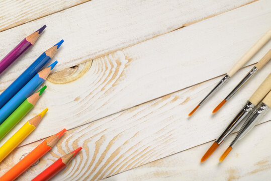 Rainbow colored pencils and paintbrushes on light wooden background