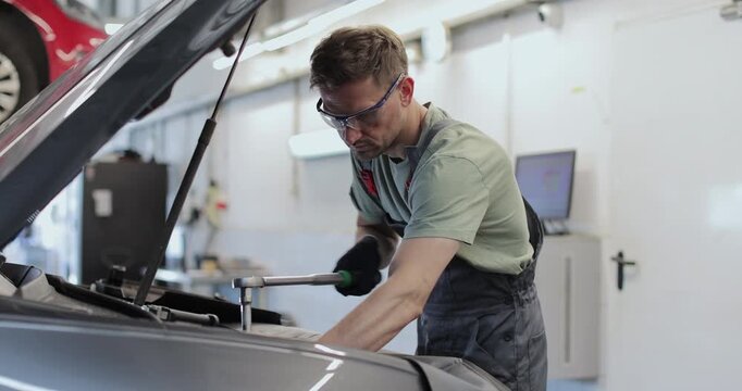 Professional mechanic working on a vehicle in a car service. Engine specialist fixing the motor. Repairman is wearing gloves and using a ratchet.