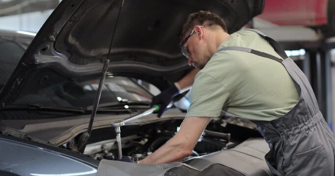 Professional mechanic working on a vehicle in a car service. Engine specialist fixing the motor. Repairman is wearing gloves and using a ratchet.