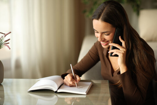 Happy woman writing in a paper agenda making phone call