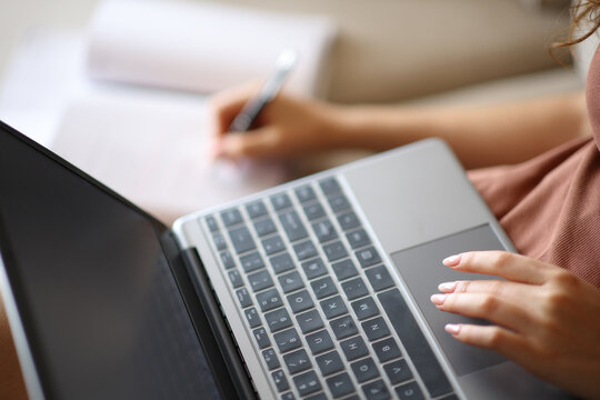 Woman hand using laptop and taking notes in notebook or agenda