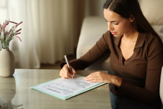 Woman signing paper form on a coffee table in a house